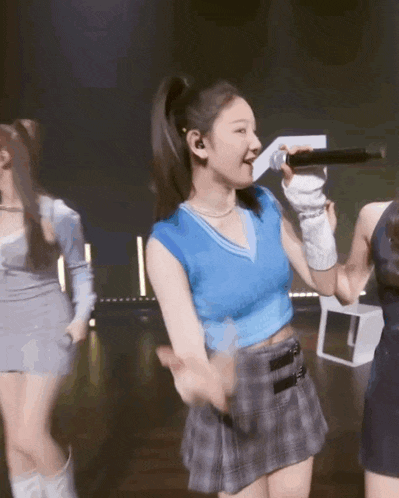 a woman in a blue top is singing into a microphone while dancing on a stage .
