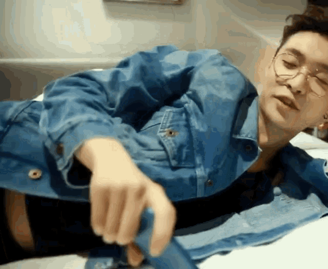 a man wearing glasses and a blue denim jacket is laying down on a bed