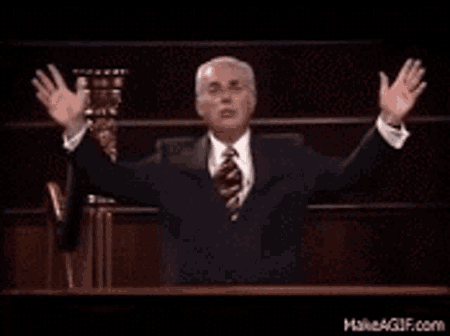 a man in a suit and tie is standing at a podium with his arms outstretched