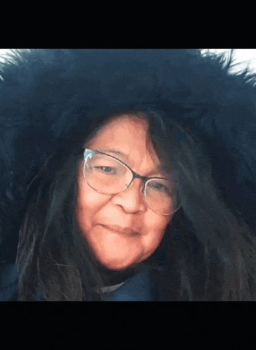 a woman wearing glasses and a fur hood is smiling