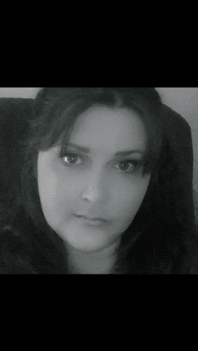 a woman is sitting in a chair and looking at the camera in a black and white photo .