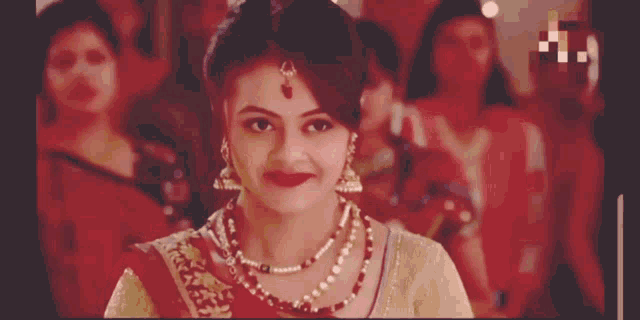a woman wearing a pearl necklace smiles in front of a group of women