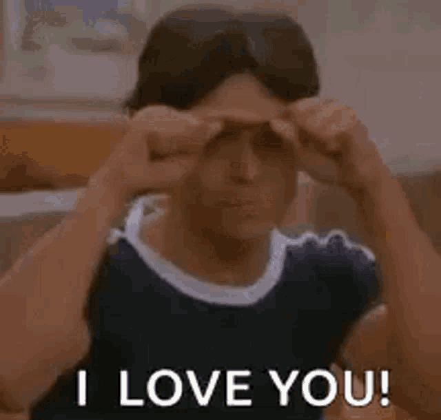 a young man is making a heart shape with his hands while sitting on a couch .