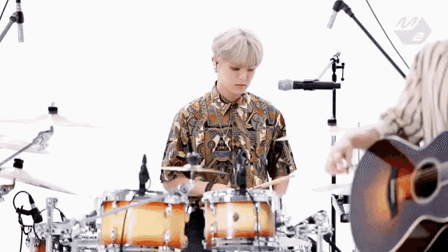 a man is playing drums while a woman is playing a guitar .