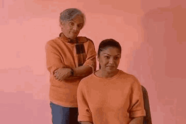 two women are standing next to each other on a pink background .