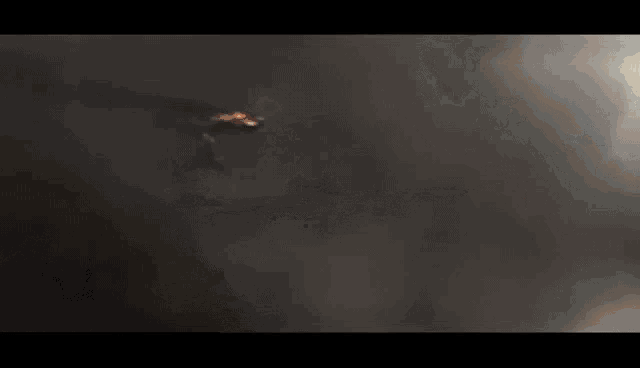 a jet is flying through a cloudy sky with a flame coming out of it .