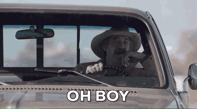a man in a cowboy hat is driving a truck and the word oh boy is on the windshield