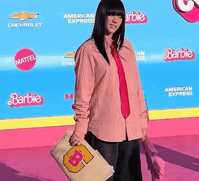 a woman in a pink shirt and red tie is standing in front of a barbie banner