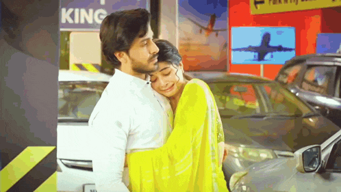a man in a white shirt is hugging a woman in a yellow saree in a parking lot