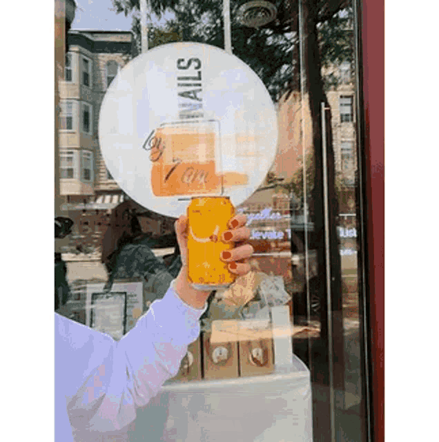 a woman with red nails is holding a can of orange juice in front of a sign that says by nails