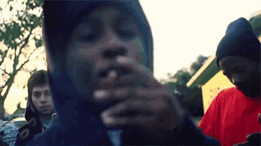 a man in a hooded jacket is smoking a cigarette in front of a group of people