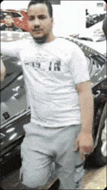 a man in a white shirt and grey shorts is kneeling in front of a car