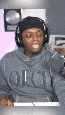 a man wearing headphones and a grey sweatshirt with the word ofcl on it
