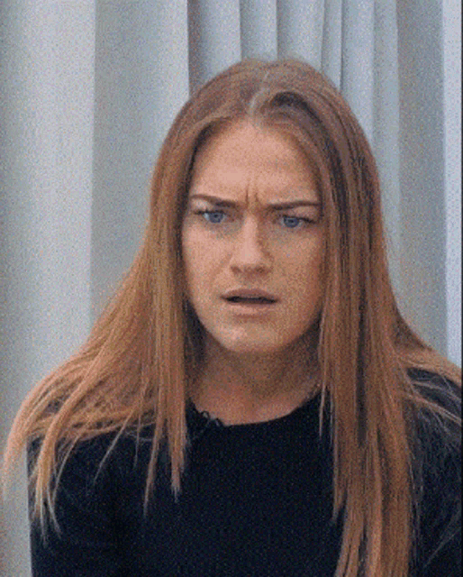 a woman with long red hair and blue eyes making a face