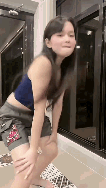 a girl in a blue tank top and shorts is standing in front of a window .