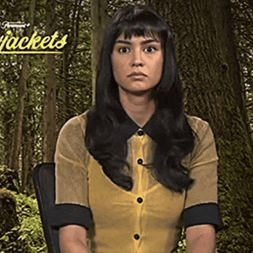 a woman in a yellow shirt is sitting in a chair in front of a sign that says " jackets "