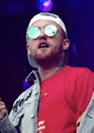 a man wearing sunglasses and a headband is singing into a microphone on stage .