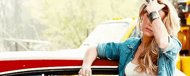 a woman in a denim shirt is standing next to a car .