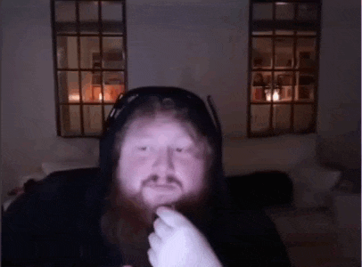 a man with a beard is sitting on a couch in front of a window .
