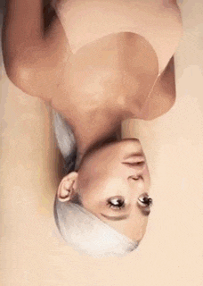 ariana grande is laying upside down on a bed wearing a tan bra .