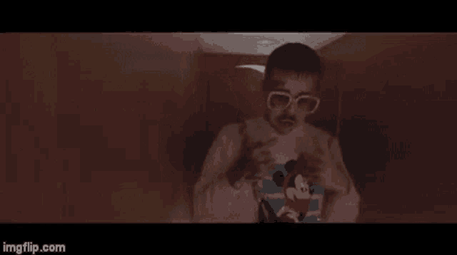 a man wearing sunglasses and a mickey mouse sweater is standing in a room .