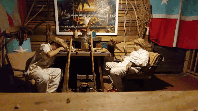 two men sit at a table with a painting on the wall