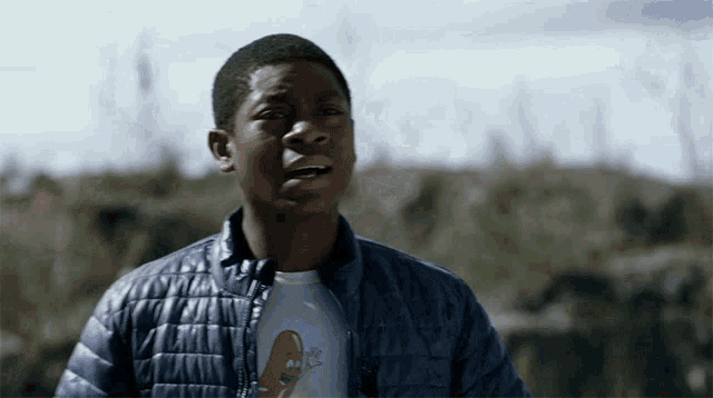 a young man wearing a blue jacket and a t-shirt with a football on it looks surprised