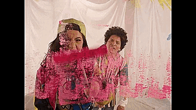 a woman and a man are standing next to each other in front of a white curtain covered in pink paint .