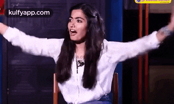 a woman is sitting in a chair with her arms outstretched and a microphone in her mouth .