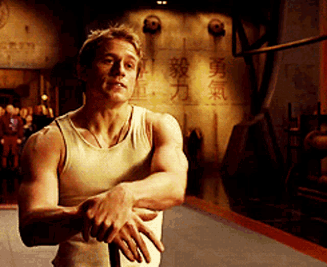 a man in a tank top is standing in front of a wall with chinese characters on it