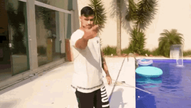 a man is standing in front of a swimming pool and pointing at the camera .