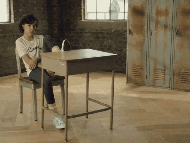 a girl sits at a desk wearing a t-shirt that says cook