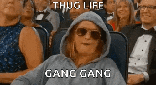 a woman in a hoodie and sunglasses is sitting in a crowd of people at a movie theater .