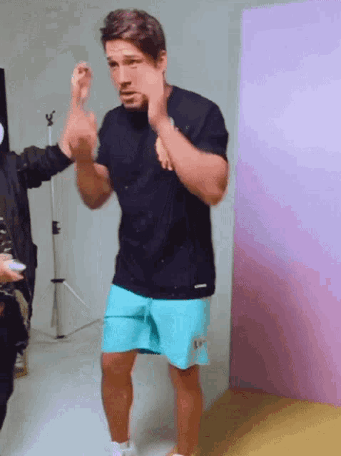a man wearing blue shorts and a black shirt is standing in front of a pink wall