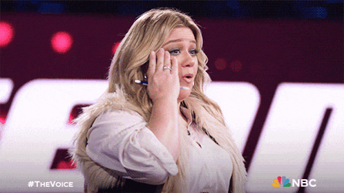 a woman with a ring on her finger talks on a cell phone in front of a sign that says nbc
