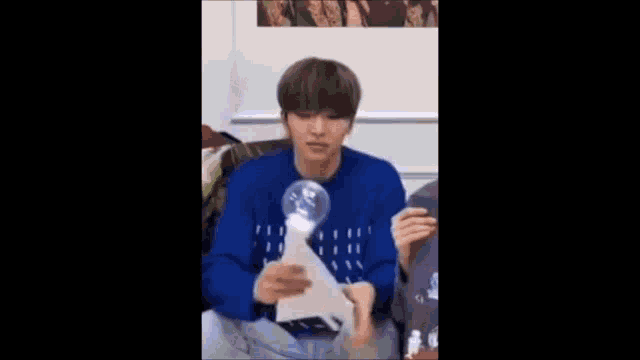 a young man in a blue sweater is holding a paper and a light bulb .