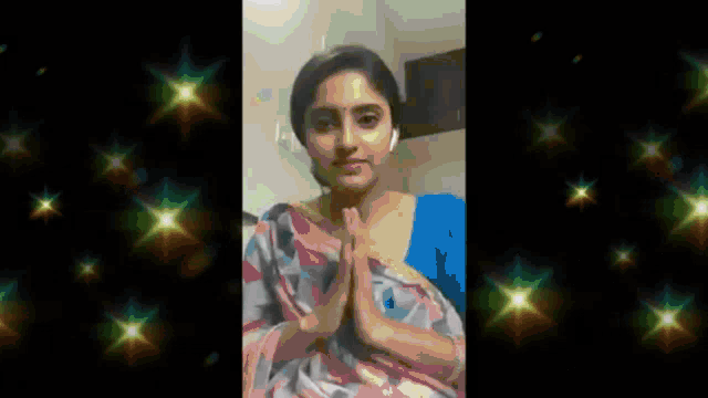 a woman in a blue shirt and a pink and white saree is wearing headphones and making a prayer gesture .
