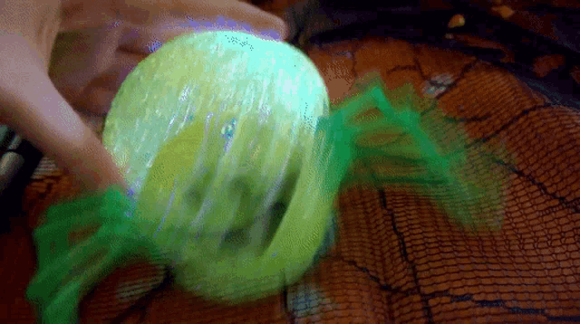 a person is holding a green ball with a spider web around it