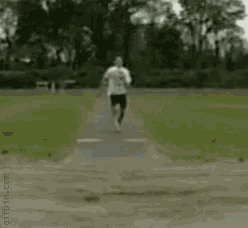 a dog is doing a handstand on a dirt road in a park .
