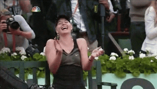 a woman is sitting on a bench laughing and clapping while a cameraman takes a picture