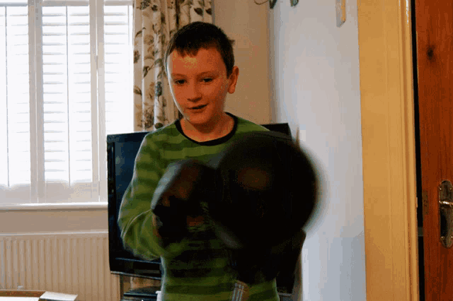 a young boy wearing boxing gloves is standing in front of a television