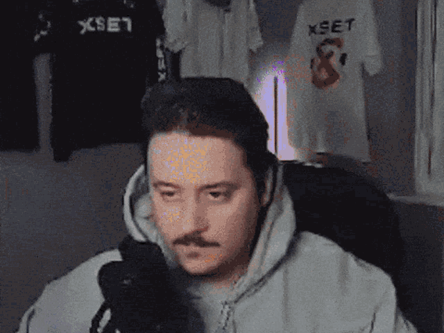 a man with a mustache is sitting in front of a microphone in front of a xset t-shirt