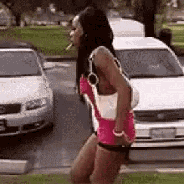 a woman is smoking a cigarette while walking down the street in front of a car .