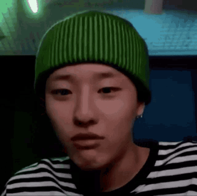 a young man wearing a green beanie and a striped shirt is making a face .
