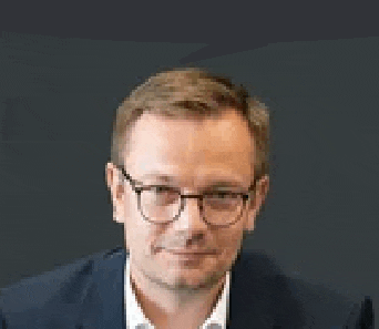 a man wearing glasses and a suit is sitting in front of a dark background .