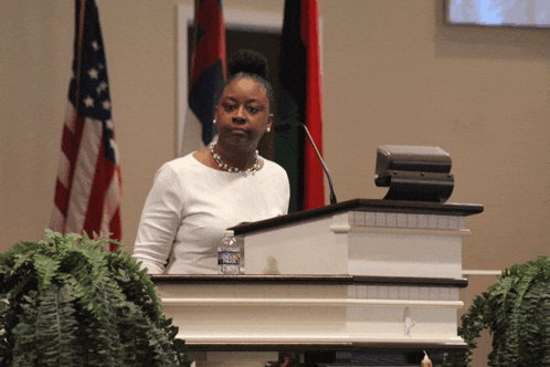 a woman stands behind a podium with a bottle of aquafina water on it