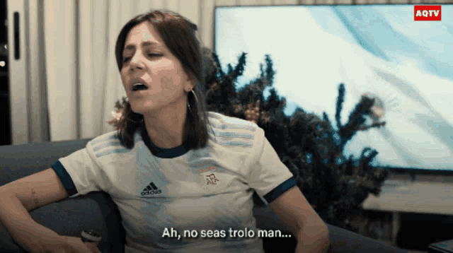 a woman wearing an adidas shirt is sitting on a couch with her mouth open