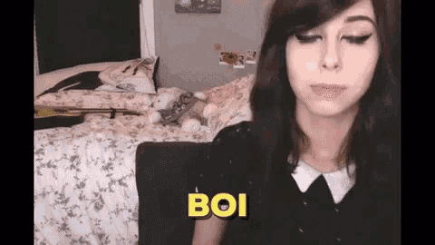 a woman is sitting in front of a bed with the word boi written on the screen