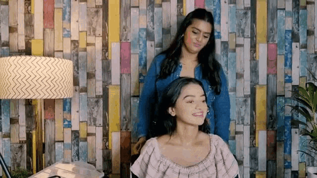 two women are sitting in front of a wooden wall .