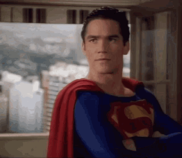 a man dressed as superman is standing in front of a window .